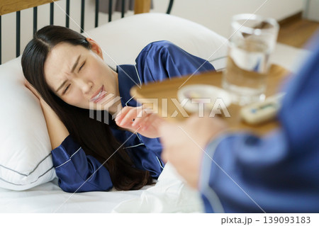 ベッドで咳き込む女性と薬を持ってくる男性の手 139093183