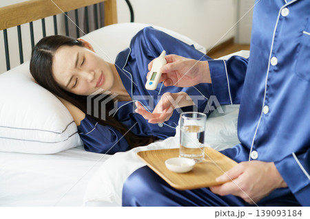 ベッドで咳き込む女性に薬と体温計を持ってくる男性の手 139093184