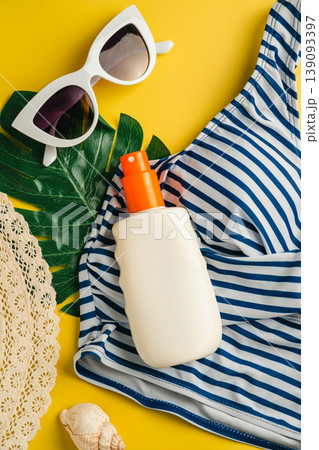 Sunscreen skin protection. Summer holiday flat lay yellow background. Beach travel accessories for vacation. Sunglasses, sun hat, swim suit, sunscreen. 139093397