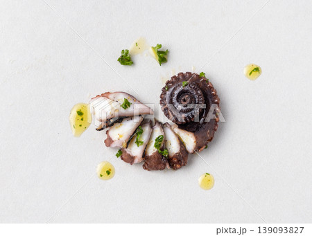 Boiled octopus sliced tentacles on plate top view. Olive oil and parsley dressing. Fresh seafood dish 139093827