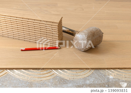 Beige oak parquet planks, rubber mallet and pencil on floor during hardwood flooring installation Beige oak parquet planks, rubber mallet and pencil on floor during hardwood flooring installation 139093831