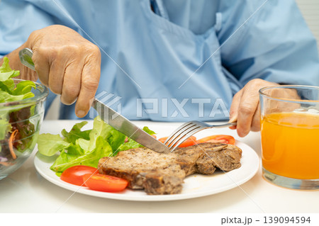 Asian elderly woman patient eating pork chop stake and vegetable salad for healthy food in hospital. Asian elderly woman patient eating pork chop stake and vegetable salad for healthy food in hospital. 139094594