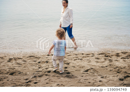 Mother and Toddler Walking on Sandy Beach Together at Calm Seaside Shore Mother and Toddler Walking on Sandy Beach Together at Calm Seaside Shore 139094749
