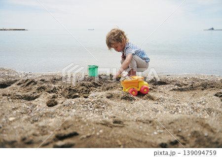 Young Boy Playing With Toy Truck and Bucket on Sandy Beach by Calm Sea Young Boy Playing With Toy Truck and Bucket on Sandy Beach by Calm Sea 139094759