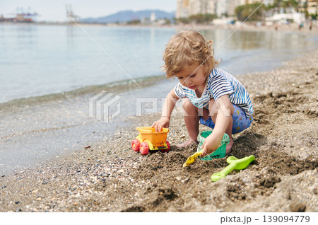 Toddler Playing With Sand Toys On Beach Near Waterline On Sunny Day 139094779