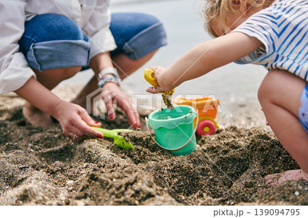 Child and Parent Playing With Bucket and Shovel on Sandy Beach 139094795