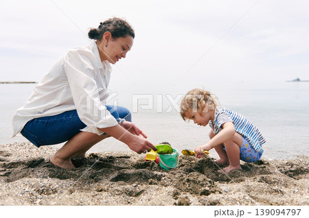 Mother and Toddler Playing With Sand Toys on a Calm Beach Mother and Toddler Playing With Sand Toys on a Calm Beach 139094797