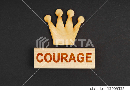 On a black surface there is a wooden crown and a block with the inscription - Courage 139095324