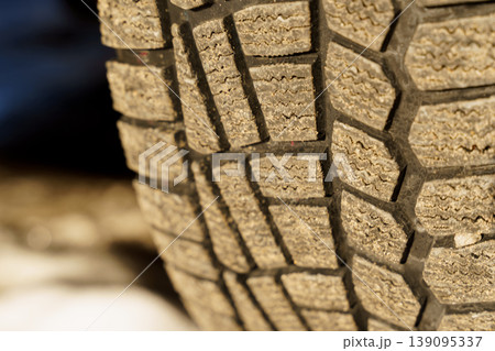 Close-up of the tread of a winter car tire on the road in winter. Close-up of the tread of a winter car tire on the road in winter. 139095337
