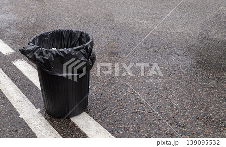 Black plastic garbage trash bin bag on gray asphalt road surface with white line marking outdoors Black plastic garbage trash bin bag on gray asphalt road surface with white line marking outdoors 139095532