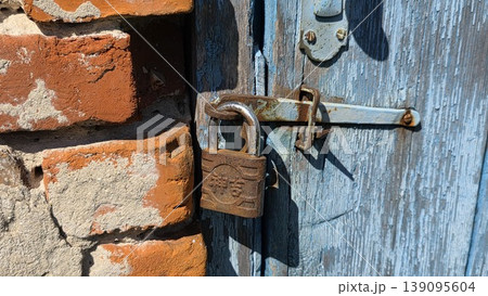 Old blue wooden door with rusty padlock and brick wall detail, weathered architectural background for security, abandonment, vintage and urban themes. 139095604