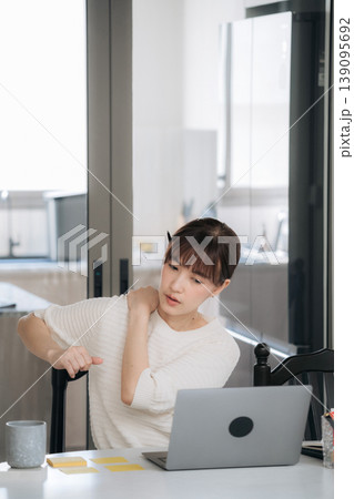 Exhausted young asian woman sitting alone at home working on modern business using digital technology and studying online feeling stressed tired and experiencing severe shoulder pain Exhausted young asian woman sitting alone at home working on modern business using digital technology and studying online feeling stressed tired and experiencing severe shoulder pain 139095692