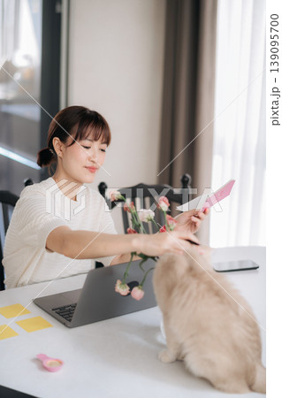Happy young asian woman working at home using modern technology for studying online business while petting cute cat feeling deeply relaxed and content during peaceful morning 139095700