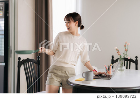 Happy asian woman cooking meal at home while working and studying online business courses using modern technology tablet device for successful multitasking lifestyle Happy asian woman cooking meal at home while working and studying online business courses using modern technology tablet device for successful multitasking lifestyle 139095722