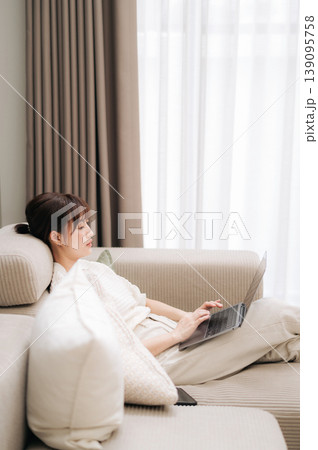 Relaxed and focused asian woman working from home using modern technology while studying online for business and resting comfortably on cozy light sofa Relaxed and focused asian woman working from home using modern technology while studying online for business and resting comfortably on cozy light sofa 139095758
