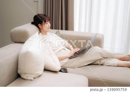 Cheerful young asian woman relaxing on comfortable sofa at home working with modern technology while studying an online business course feeling calm and happy during peaceful afternoon Cheerful young asian woman relaxing on comfortable sofa at home working with modern technology while studying an online business course feeling calm and happy during peaceful afternoon 139095759