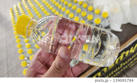 Person Holding a Clear Plastic Mineral Water Bottle with a Bright Yellow Cap 139095784