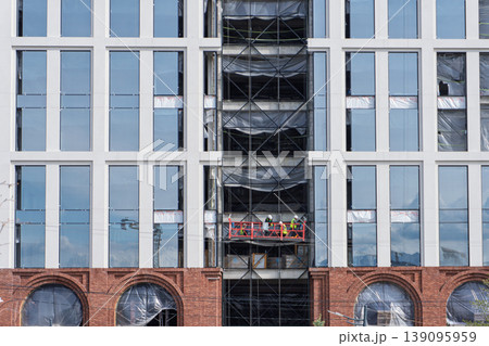 Builders on a suspended platform working on a modern glass building facade Builders on a suspended platform working on a modern glass building facade 139095959
