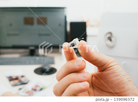 Intra-ear hearing aid close-up in a male hand. Hearing solution, a man holding a hearing aid, close-up. Intra-ear hearing aid close-up in a male hand. Hearing solution, a man holding a hearing aid, close-up. 139096372