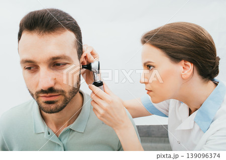 ENT doctor checking adult male ear using an otoscope. Hearing exam for mixed race man. Otitis media, ear inflammation ENT doctor checking adult male ear using an otoscope. Hearing exam for mixed race man. Otitis media, ear inflammation 139096374