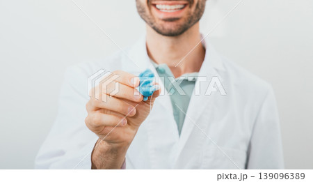 Positive audiologist holding in his hands molded individual hearing aid earmolds for his patient, close-up. Hearing solution 139096389