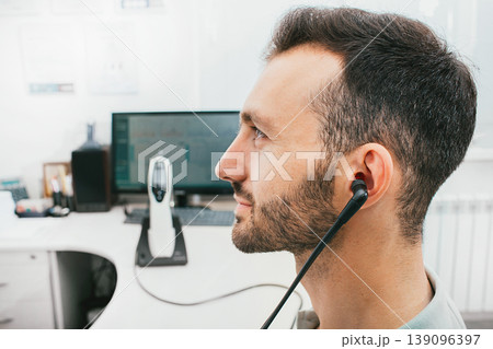 Diagnosis of hearing impairment, tympanometry, hearing test. A man during a hearing diagnostic procedure, and a special earphone in his ear. Diagnosis of hearing impairment, tympanometry, hearing test. A man during a hearing diagnostic procedure, and a special earphone in his ear. 139096397