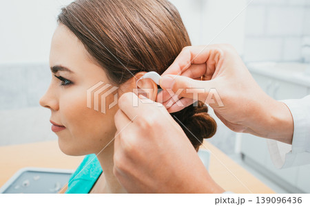 Audiologist inserting hearing aid on female ear, close-up . Deafness treatment, hearing solution 139096436