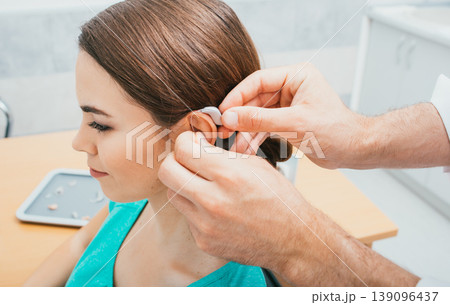 Audiologist inserting hearing aid on female ear, close-up . Deafness treatment, hearing solution 139096437