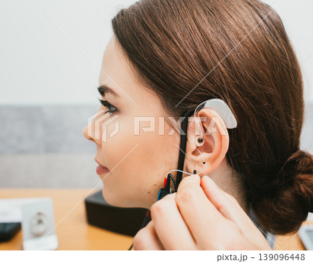 Audiologist programming hearing aid acoustic response using the software. Young woman getting hearing aid adjustments Audiologist programming hearing aid acoustic response using the software. Young woman getting hearing aid adjustments 139096448