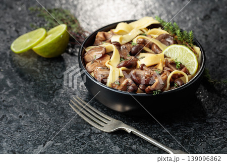 Shimeji and shiitake mushrooms stir-fried with soy sauce, garlic and thyme, served with noodles and lime slice in a black ceramic bowl. Shimeji and shiitake mushrooms stir-fried with soy sauce, garlic and thyme, served with noodles and lime slice in a black ceramic bowl. 139096862