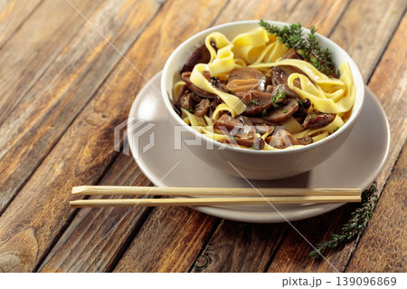 Shimeji and shiitake mushrooms stir-fried with soy sauce, garlic and thyme, served with noodles in a ceramic bowl. Shimeji and shiitake mushrooms stir-fried with soy sauce, garlic and thyme, served with noodles in a ceramic bowl. 139096869