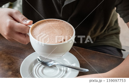 Closeup image of hands holding a cup of hot chocolate on rustic wooden background Closeup image of hands holding a cup of hot chocolate on rustic wooden background 139097753
