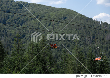Empty chairlift ascending over a lush green mountain forest. 139098962