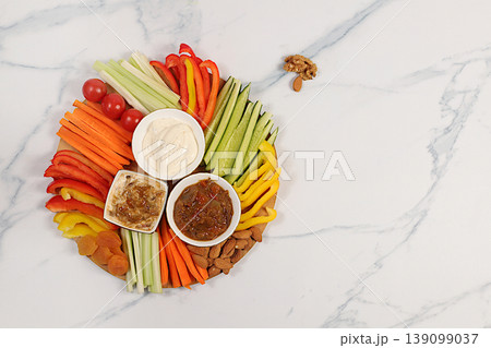Healthy food kitchen background with hummus bowl and raw vegetable sticks, nuts and dried apricots. Hummus platter with appetizers, Middle Eastern plate, traditional vegan snacks, Healthy food kitchen background with hummus bowl and raw vegetable sticks, nuts and dried apricots. Hummus platter with appetizers, Middle Eastern plate, traditional vegan snacks, 139099037