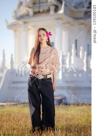 Trendy Thai fashion woman wearing a traditional Sabai paired with denim jeans at temple, reflecting the growing fashion trend in Thailand that blends cultural heritage with contemporary street style. 139100185
