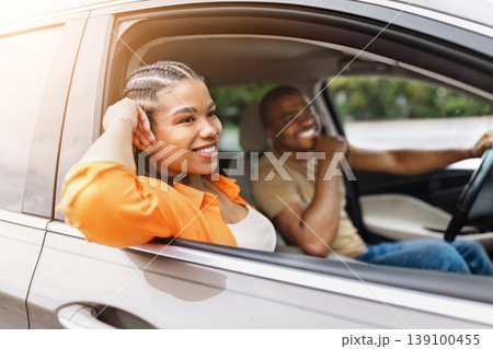 Relaxed black woman leaning out of car window while traveling with partner 139100455