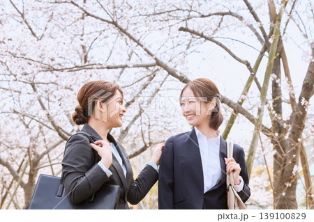 桜並木の下で笑顔で会話する二人のリクルートスーツ姿の若い女性・新入社員・就職活動イメージ 桜並木の下で笑顔で会話する二人のリクルートスーツ姿の若い女性・新入社員・就職活動イメージ 139100829