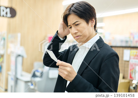 レシートの値段を見て不満を抱く男性 レシートの値段を見て不満を抱く男性 139101458