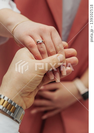 Hands Clasped Together Displaying Fresh Engagement Ring In Focus. Detailed View Of Intertwined Fingers Highlighting Newly Placed Engagement Jewelry Piece Amid Blurred Background 139102518