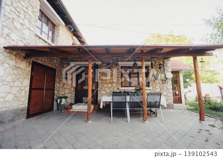 Outdoor Covered Dining Area With Table And Chairs Under Wooden Pergola, Shaded Setting For Casual Meals, Wicker Seating, Lantern Accent And Paved Floor Creating Cozy Hospitality Scene Outdoor Covered Dining Area With Table And Chairs Under Wooden Pergola, Shaded Setting For Casual Meals, Wicker Seating, Lantern Accent And Paved Floor Creating Cozy Hospitality Scene 139102543