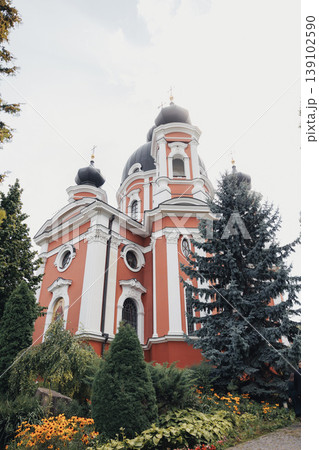 Ornate Red Orthodox Church Exterior Framed By Evergreens, Baroque Towers With Cupola Silhouettes Rising Above Manicured Gardens, Textured Stucco Facade, Decorative Cornices, Tranquil Ornate Red Orthodox Church Exterior Framed By Evergreens, Baroque Towers With Cupola Silhouettes Rising Above Manicured Gardens, Textured Stucco Facade, Decorative Cornices, Tranquil 139102590