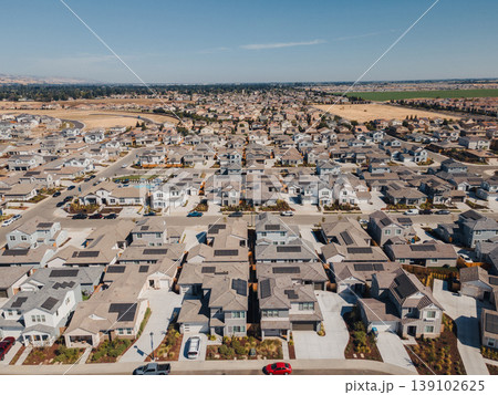 Aerial Planned Grid Community Long Perspective Revealing Symmetric Rows Of Houses, Narrow Backyards, Parked Cars, Distant Farmland, Serene Afternoon Light And Efficient Street Layout. 139102625