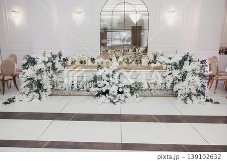 Lavish Floraladorned Wedding Head Table, Set In Elegant Ballroom With White Linens, Abundant Greenery Garlands, Cascading Roses, Crystal Candlesticks, Mirrored Backdrop Reflecting Soft Lavish Floraladorned Wedding Head Table, Set In Elegant Ballroom With White Linens, Abundant Greenery Garlands, Cascading Roses, Crystal Candlesticks, Mirrored Backdrop Reflecting Soft 139102632