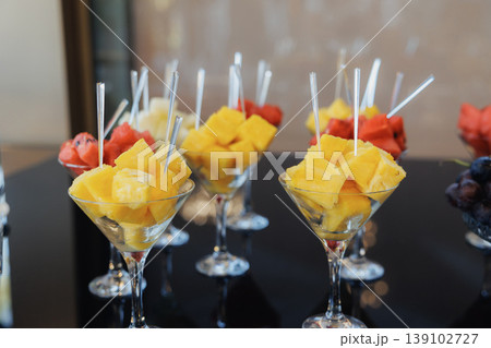 Fresh Pineapple And Watermelon Skewers Presented In Stemmed Glasses On Black Buffet Table, Vibrant Tropical Colors, Cocktail Forks, Perfect For Summer Receptions And Party Catering Fresh Pineapple And Watermelon Skewers Presented In Stemmed Glasses On Black Buffet Table, Vibrant Tropical Colors, Cocktail Forks, Perfect For Summer Receptions And Party Catering 139102727