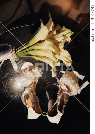 Overhead Bridal Shoes With Calla Bouquet Reflected On Dark Glass Surface, Long Stems And Crisp Petals Framing Delicate Heels, Cinematic Warm Tones And Moody Shadows Create Romantic Tableau. Overhead Bridal Shoes With Calla Bouquet Reflected On Dark Glass Surface, Long Stems And Crisp Petals Framing Delicate Heels, Cinematic Warm Tones And Moody Shadows Create Romantic Tableau. 139102745