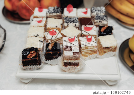 Assorted Petit Layered Cakes On Tray, Variety Of Miniature Cakes With Cream Layers, Chocolate Squares And Red Decorative Accents, Displayed On White Platter For Wedding Dessert Table Assorted Petit Layered Cakes On Tray, Variety Of Miniature Cakes With Cream Layers, Chocolate Squares And Red Decorative Accents, Displayed On White Platter For Wedding Dessert Table 139102749