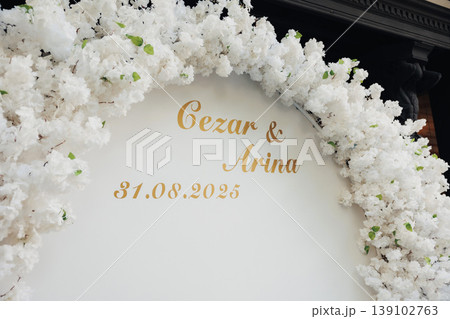 Wedding Floral Arch Backdrop Gold Lettering Elegant White Blooms Framing Circular Sign Bearing Couple Names And Date, Soft Natural Lighting, Modern Minimalist Styling For Intimate Garden 139102763