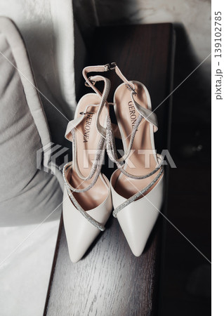 White Bridal Heels Placed On Bench, Soft Natural Light Highlighting Satin Straps And Pointed Toes, Subtle Rhinestone Detail, Muted Neutral Palette Evoking Wedding Morning Calm And Elegant 139102785