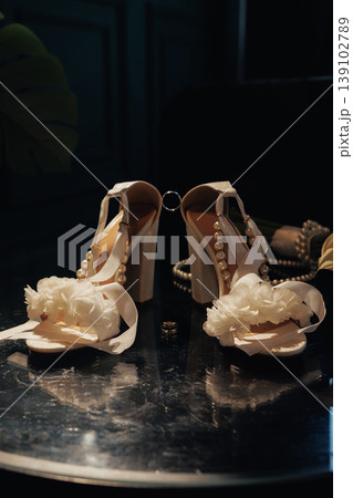 Elegant Strappy Heels With Floral Embellishment Resting On Glossy Round Table Beside Pearl Clutch, Warm Studio Lighting Emphasizes Satin Straps And Ornate Buckle, Fashion Still Life 139102789