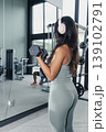 Woman Performing Dumbbell Curl Wearing Headphones, Mirror Reflection, Toned Arms, Controlled Motion, Gym Weight Rack, Mint Leggings, Concentration On Form, Strength Building, Repetition 139102791